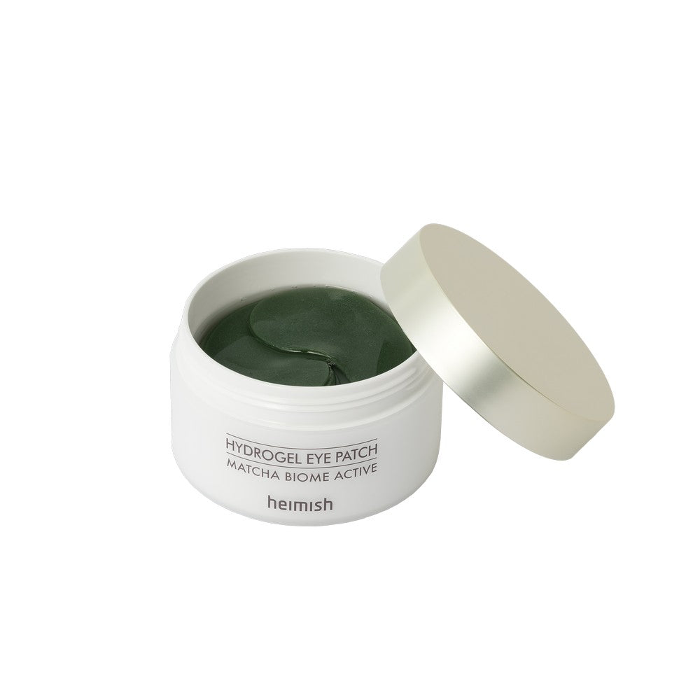 A container with Heimish Matcha Biome Hydrogel Eye Patch stickers inside. The container is open, and the stickers are visible as green hydrogel patches.